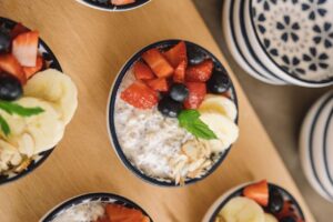 Overhead view of oatmeal bowls topped with fresh fruits like bananas, strawberries, and blueberries.