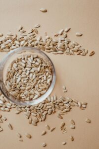 Glass jar filled with raw sunflower seeds on a beige surface. Ideal for health and nutrition themes.