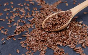 Close-up of brown flax seeds scattered with wooden spoon on slate.